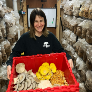 A vendor holding a box of assorted mushrooms