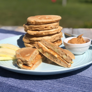 A stack of pancakes on a plate with two pancakes turned into a pancake sandwich with peanut butter and apples