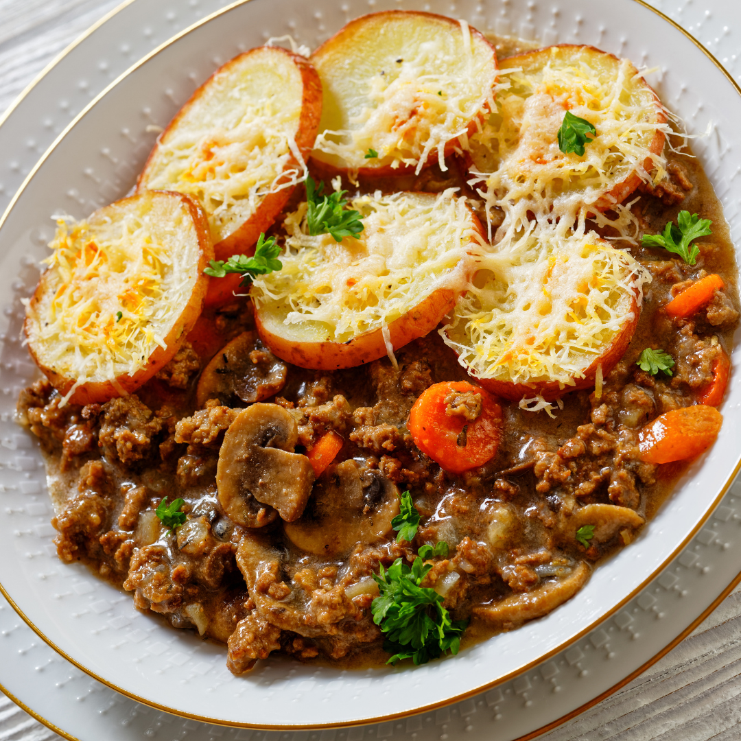 Bowl of ground beef and vegetables topped with sliced, cooked potatoes and cheese