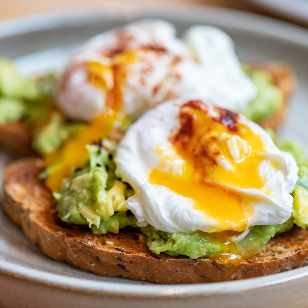 open breakfast sandwich with guacamole, poached egg and whole grain bread